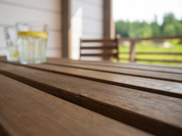 Garden furniture table and chair on the terrace of a country house, hotel. Two glasses with a refreshing drink with a lemon in the distance, blurred, on a wooden table. Horizontal orientation, space