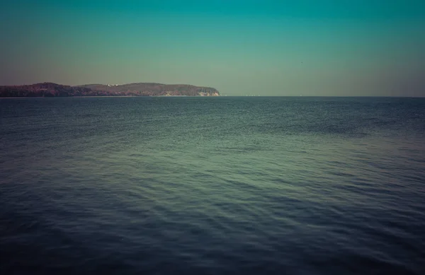 calm sea with small waves during sunny day with a coast with cliffs on a shore