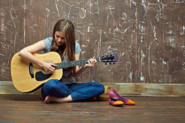 Genç kadın yerde otururken akustik gitar çalmak 