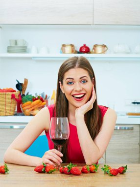 Mutfakta oturup kırmızı şarap cam ile gülümseyen genç kadın 