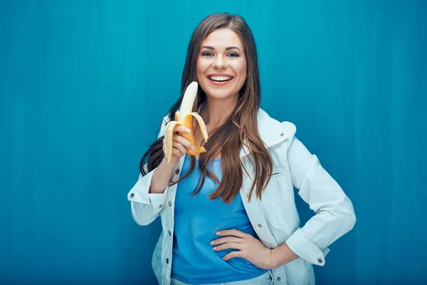 Smilende Kvinde Spiser Banan Mens Udgør Blå Væg Baggrund - Stock-foto