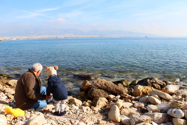 21 Aralık 2018, Pire, Attica, Yunanistan. Sahilde rahatlatıcı onun dedesi ile küçük bir çocuk. Saronic Gulf view. Popüler turistik Avrupa hedef. Manzara. Deniz manzarası