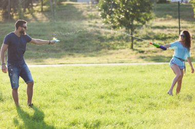 Birbirlerini takip ve su silahlarla oynayan bir çayır ar gün batımı oynak genç bir çift.