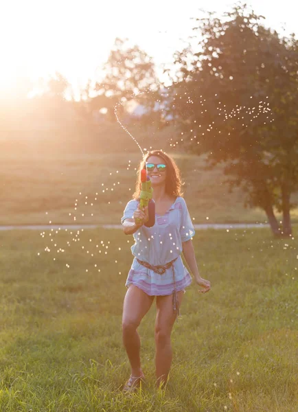 A playful young couple chasing each other and playing with water guns in a meadow ar sunset.