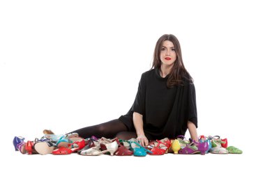 Beyaz arka planda izole edilmiş genç bir kadın. Bir sürü farklı beden ve renkte ayakkabısı var..