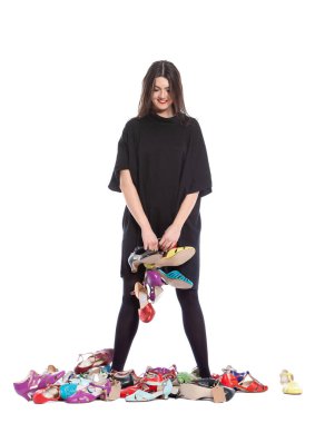 Beyaz arka planda izole edilmiş genç bir kadın. Bir sürü farklı beden ve renkte ayakkabısı var..