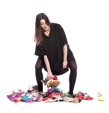 Beyaz arka planda izole edilmiş genç bir kadın. Bir sürü farklı beden ve renkte ayakkabısı var..