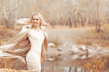 Sonbahar parkında yürüyen şık, sarışın kadın.