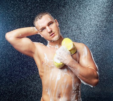 Duşa bir sünger ve duş jeli ile yakışıklı kaslı çekici genç bir adam