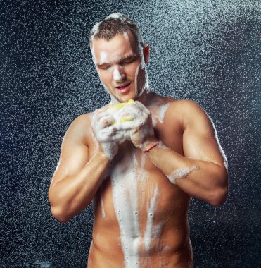 Duşa bir sünger ve duş jeli ile yakışıklı kaslı çekici genç bir adam