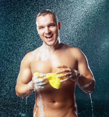 Duşa bir sünger ve duş jeli ile yakışıklı kaslı çekici genç bir adam
