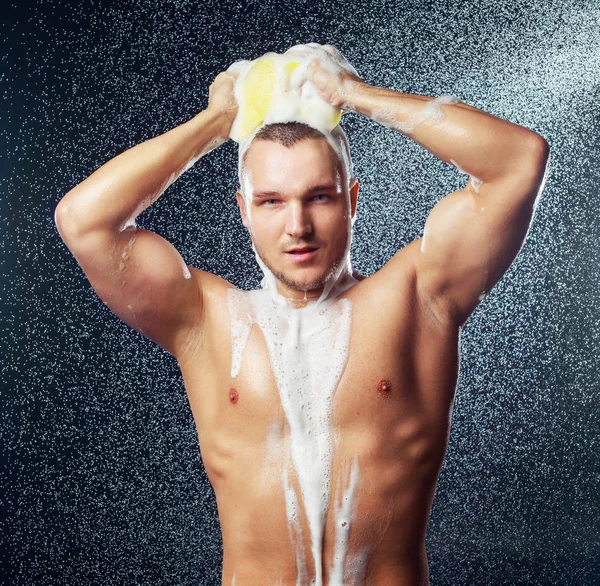 a handsome muscular attractive young man taking a shower with a sponge and shower gel