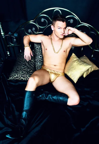 有吸引力的肌肉男人穿着金色的链子和内衣在床上与黑色亚麻布 — 图库照片