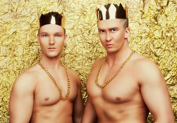 两个脱衣舞舞者穿着与金色的皇冠在演播室反对金色演播室背景 — 图库照片