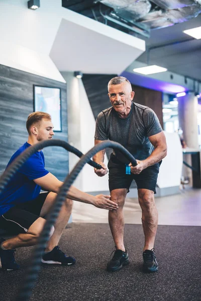 Senior man exercising with ropes at the gym. Personal training. Healthy lifestyle.