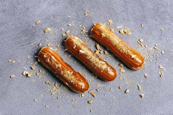 Tre Eclairs Caramello Sul Bancone Grigio Con Spruzzi Oro Intorno — Foto Stock