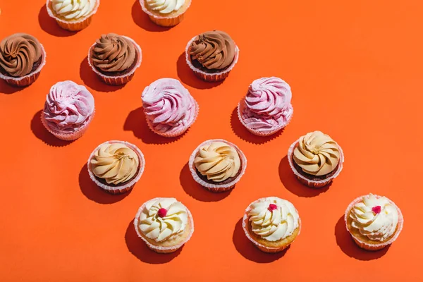 五颜六色的纸杯蛋糕成排在橙色的背景 甜品甜点 — 图库照片