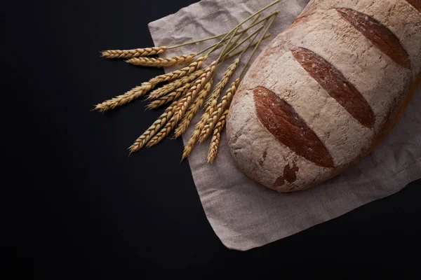Loaf of bread with ears of wheat on black background