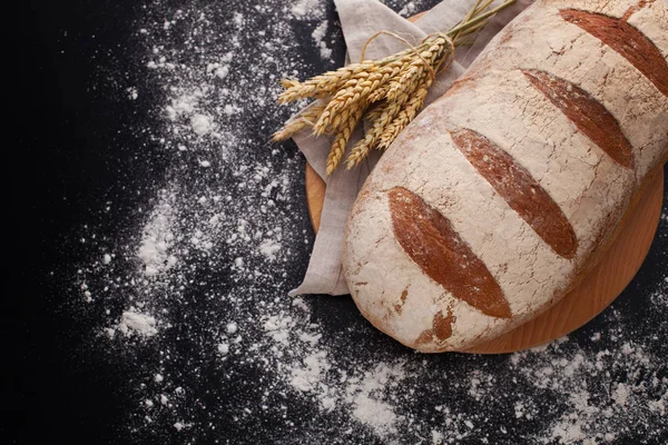 Loaf of bread with ears of wheat on black background