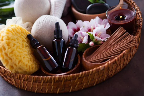 herbal compress balls with spa pebbles and hibiscus flowers with on aromatherapy oil bottles in wicker tray