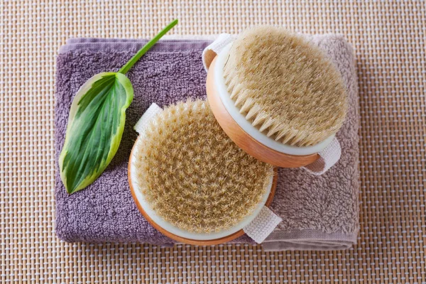 two brushes for dry body massage on towels and green leaf, beauty treatment