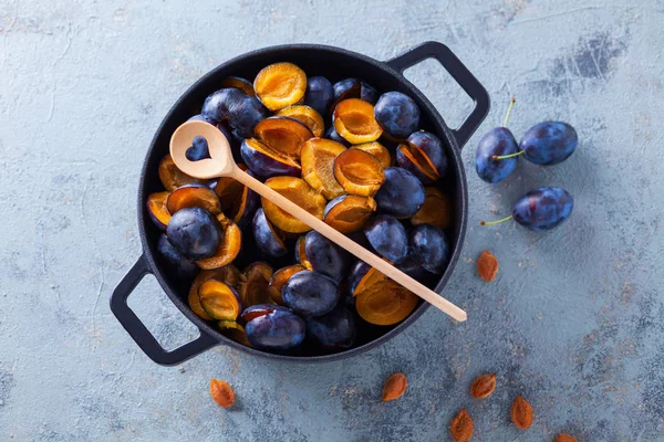 Cast iron pot with wooden spoon full of plums on marble background with bones.