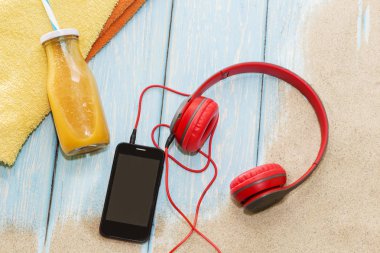 Kulaklık ve güneş gözlüklü telefon mavi arka planda, bir yaz plajında.