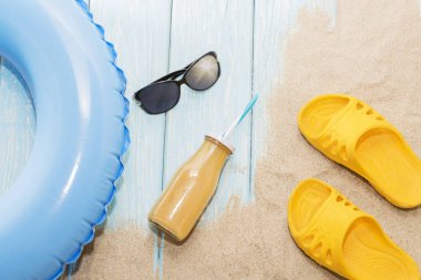 Sahilde yaz tatili. Sarı parmak arası terlik ve yüzme daireler, suyu şişesi ve güneş gözlüğü