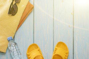 Bir şişe su ve parlak havlular, mavi arka planda sarı bir tahta ve güneş gözlüğü. Boşluğu Kopyala