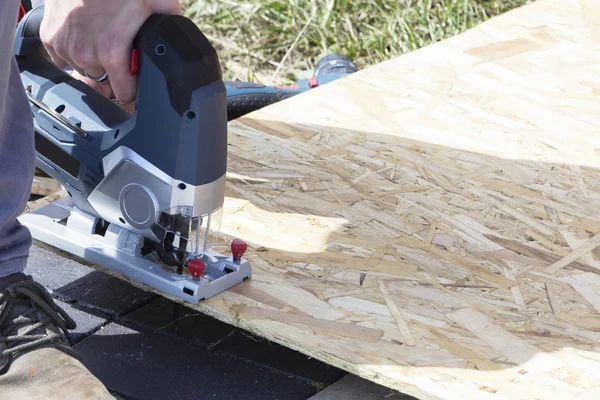 Genç bir işçi sokakta kontrplak bir elektrikli testere ile bir parça keser.