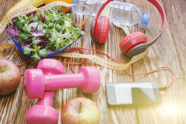 Ahşap bir tezgah, diyet ve sağlıklı beslenme kavramı dumbbells ile taze organik sebze. Kulaklık ve telefon. Müzik spor