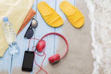Kulaklık ve güneş gözlüklü telefon mavi arka planda, bir yaz plajında..