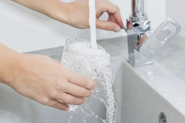 Hand holding a glass of water poured from the kitchen faucet. — Stock Photo, Image