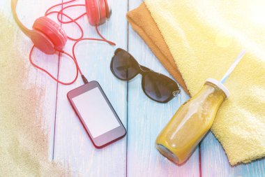 Kulaklık ve güneş gözlüklü telefon mavi arka planda, bir yaz plajında..