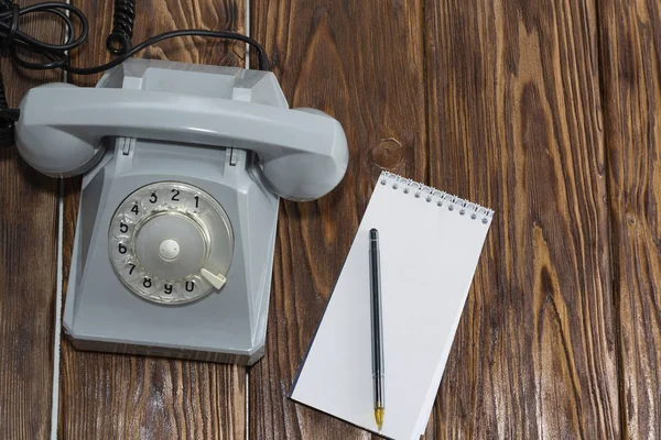 vintage grey phone, writing pad on wooden background close-up, top view