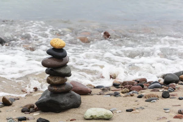 Uma pirâmide de pedras com uma pedra brilhante no topo fica na praia arenosa. O conceito de liderança Fotografias De Stock Royalty-Free