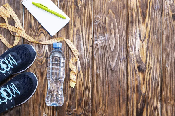 Estilo de vida saludable y antecedentes deportivos. Zapatos deportivos, bloc de notas y bolígrafo, y botella de agua sobre fondo de madera con copyspace, vista superior . —  Fotos de Stock