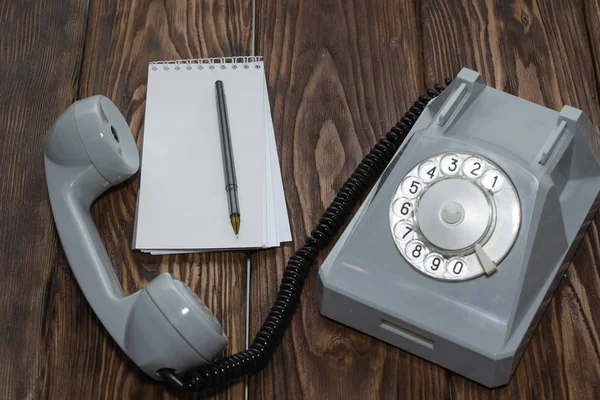 vintage grey phone, writing pad on wooden background close-up, top view