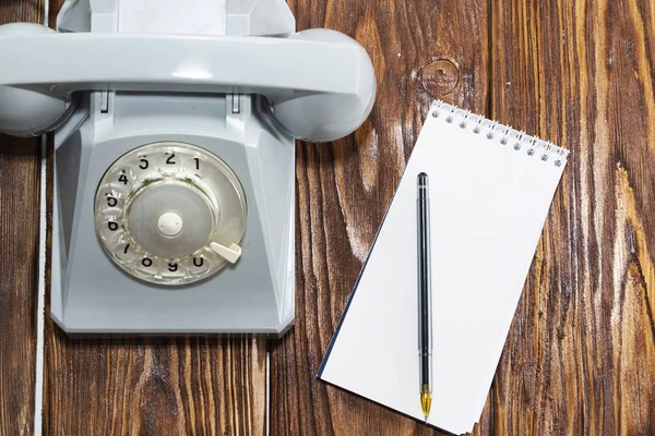 vintage grey phone, writing pad on wooden background close-up, top view