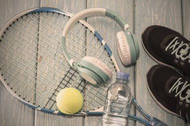 Tenis raketi. Açık mavi arkaplan. Spor ayakkabıları, roket, top, su şişesi, müzik kulaklıkları..