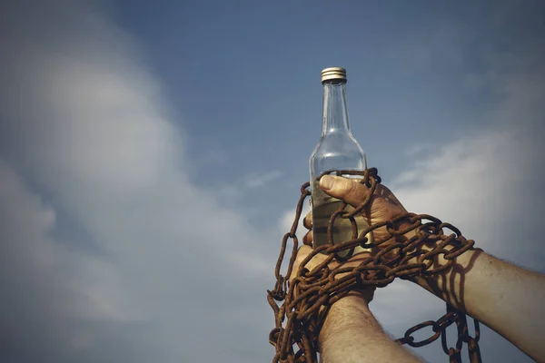 Bir şişe alkol, mavi gökyüzü karşı zincirlenmiş el — Stok fotoğraf