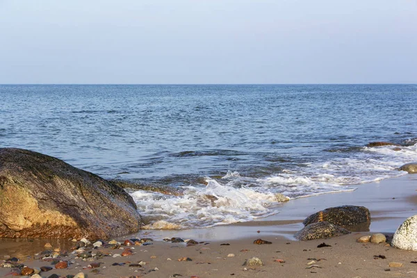 Una hermosa ola golpea las rocas en una playa de arena en un día soleado . —  Fotos de Stock