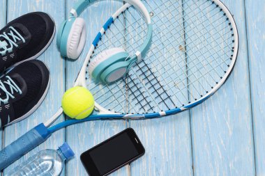 Tenis raketi. Açık mavi arkaplan. Spor ayakkabıları, roket, top, su şişesi, müzik kulaklıkları..