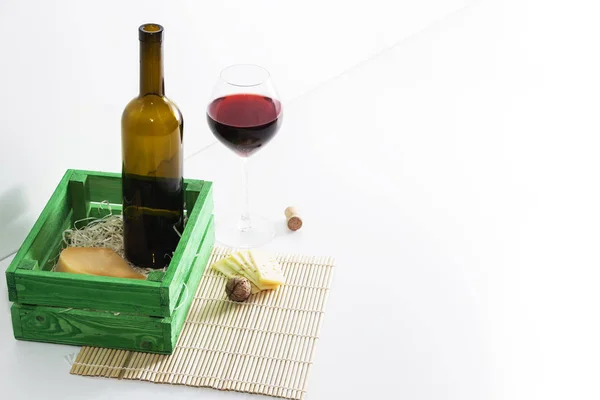 A bottle of red wine with a glass and a piece of cheese. — Stock Photo, Image