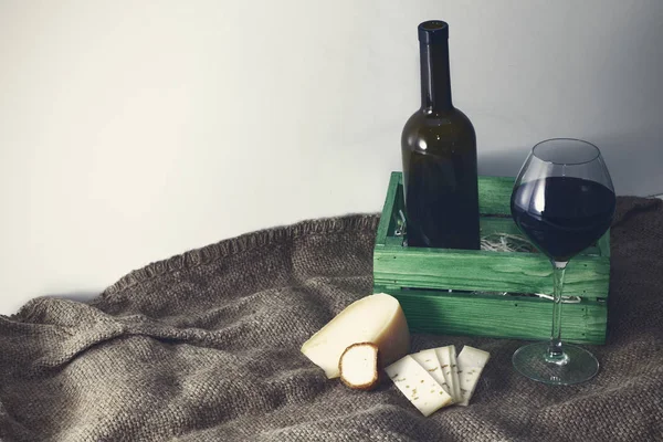 A bottle of red wine with a glass and a piece of cheese. — Stock Photo, Image