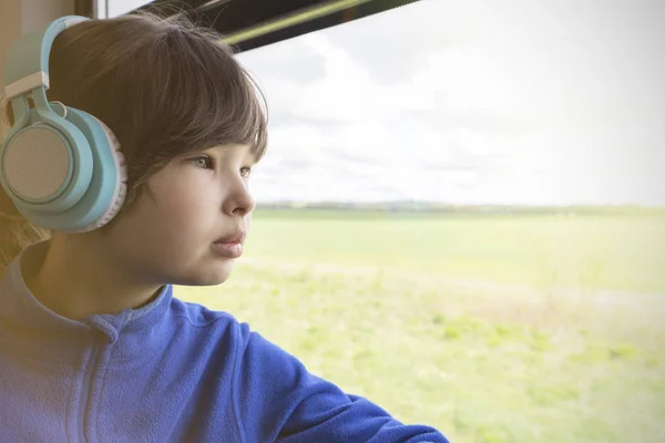 Flickan tittar ut genom fönstret på tåget och lyssnar på musik i hörlurar. — Stockfoto