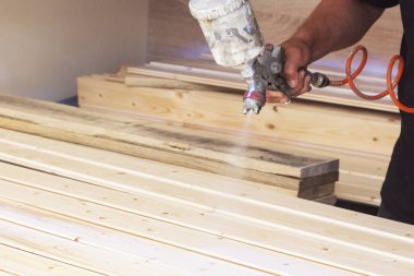 Bir adam bir sprey ile atölyede vernik ile ahşap panoları kapsar.