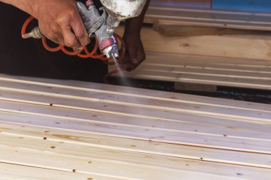 Bir adam bir sprey ile atölyede vernik ile ahşap panoları kapsar.