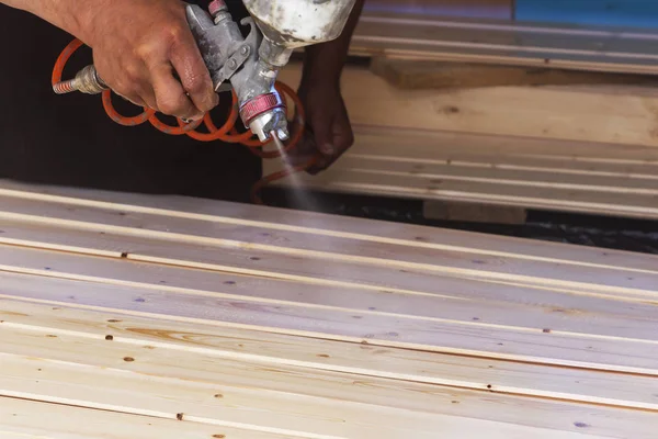 Bir adam bir sprey ile atölyede vernik ile ahşap panoları kapsar.