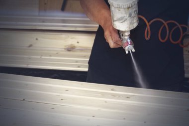 Bir adam bir sprey ile atölyede vernik ile ahşap panoları kapsar.